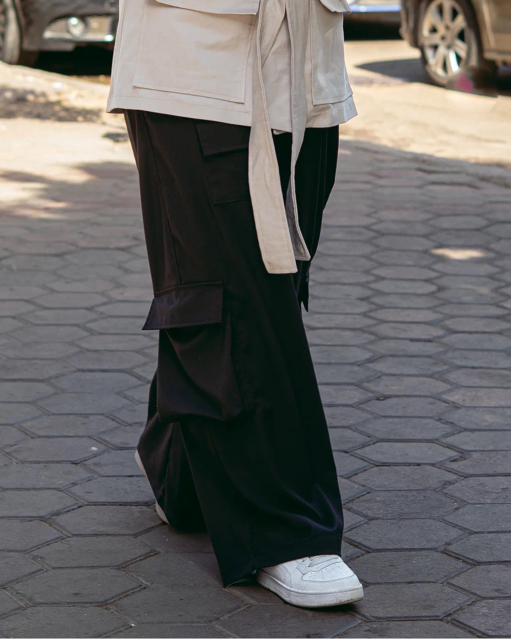 Woman in a beige coat and hijab using a phone on a city street.