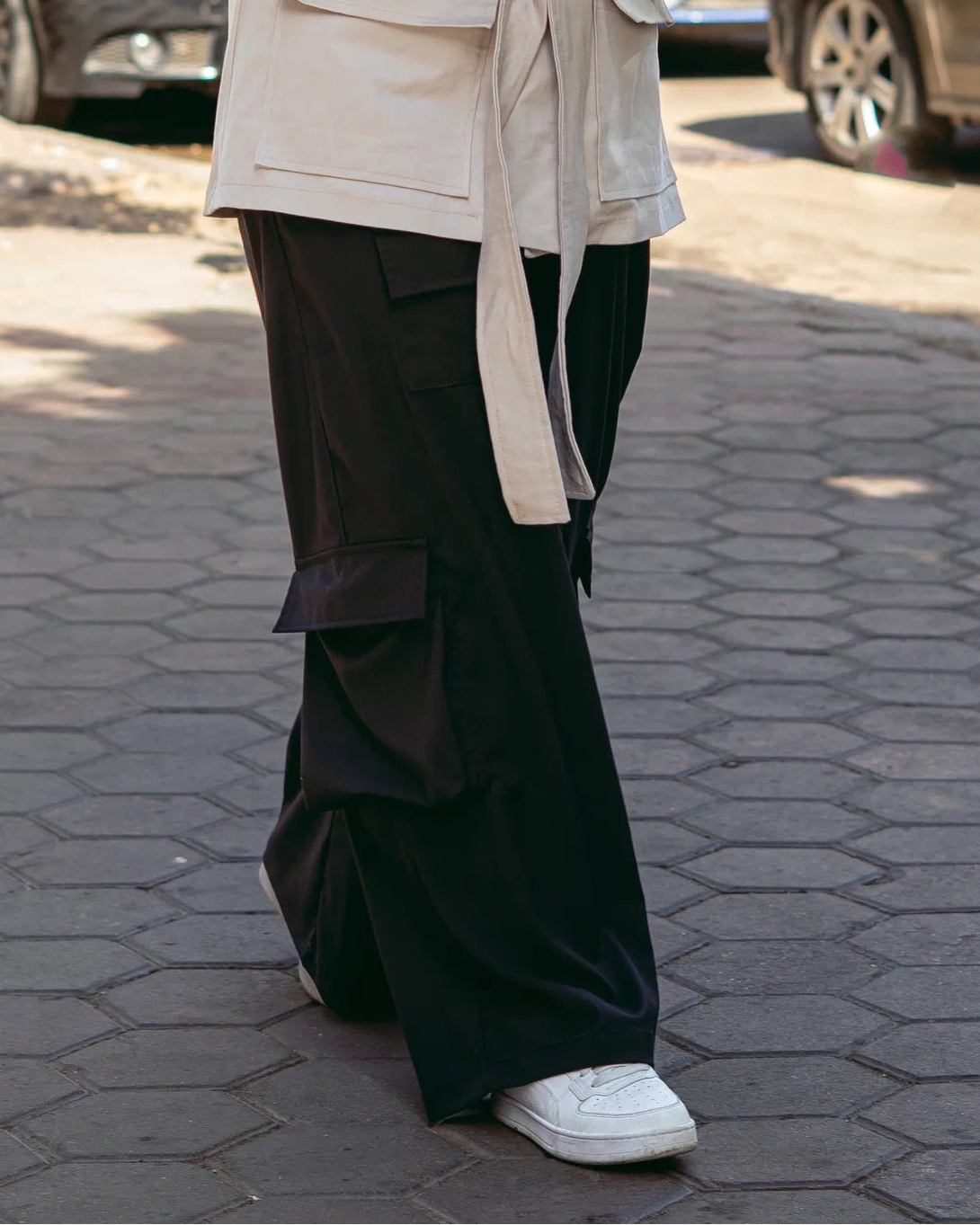 Woman in a beige coat and hijab using a phone on a city street.