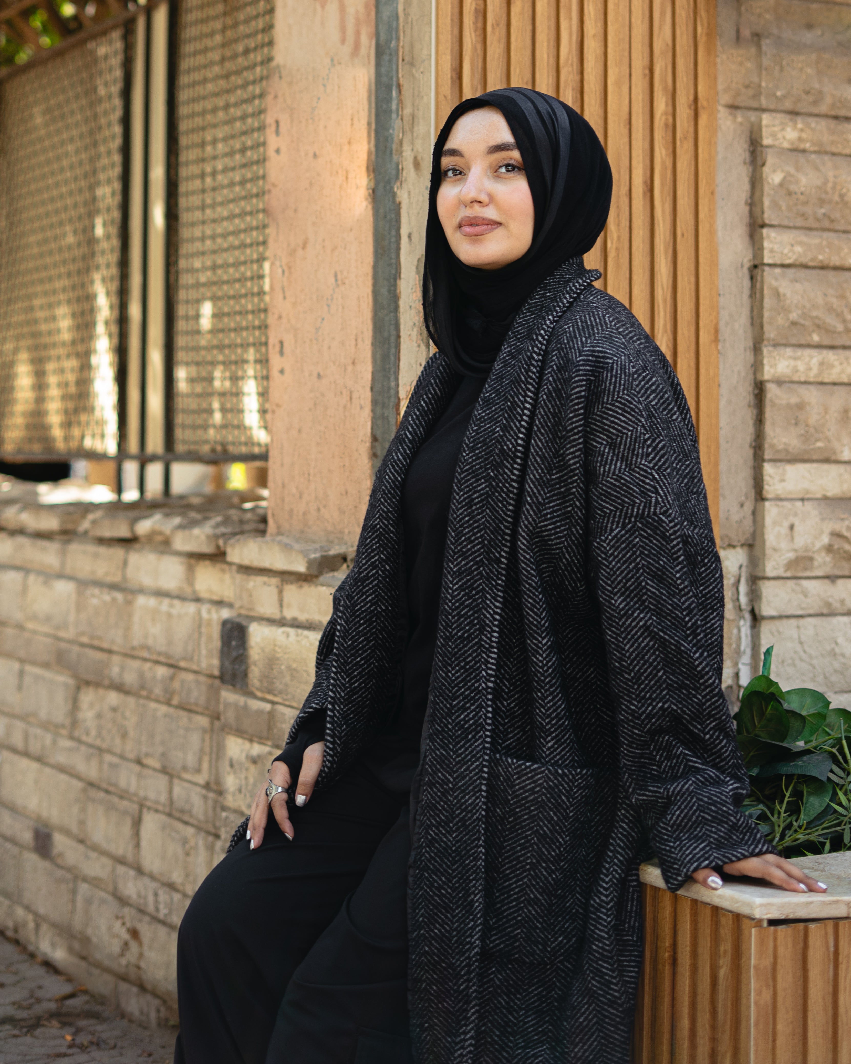 Woman wearing a black hijab and dark gray cardigan standing outdoors.