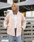 Woman wearing a beige jacket and hijab standing outdoors with blurred background