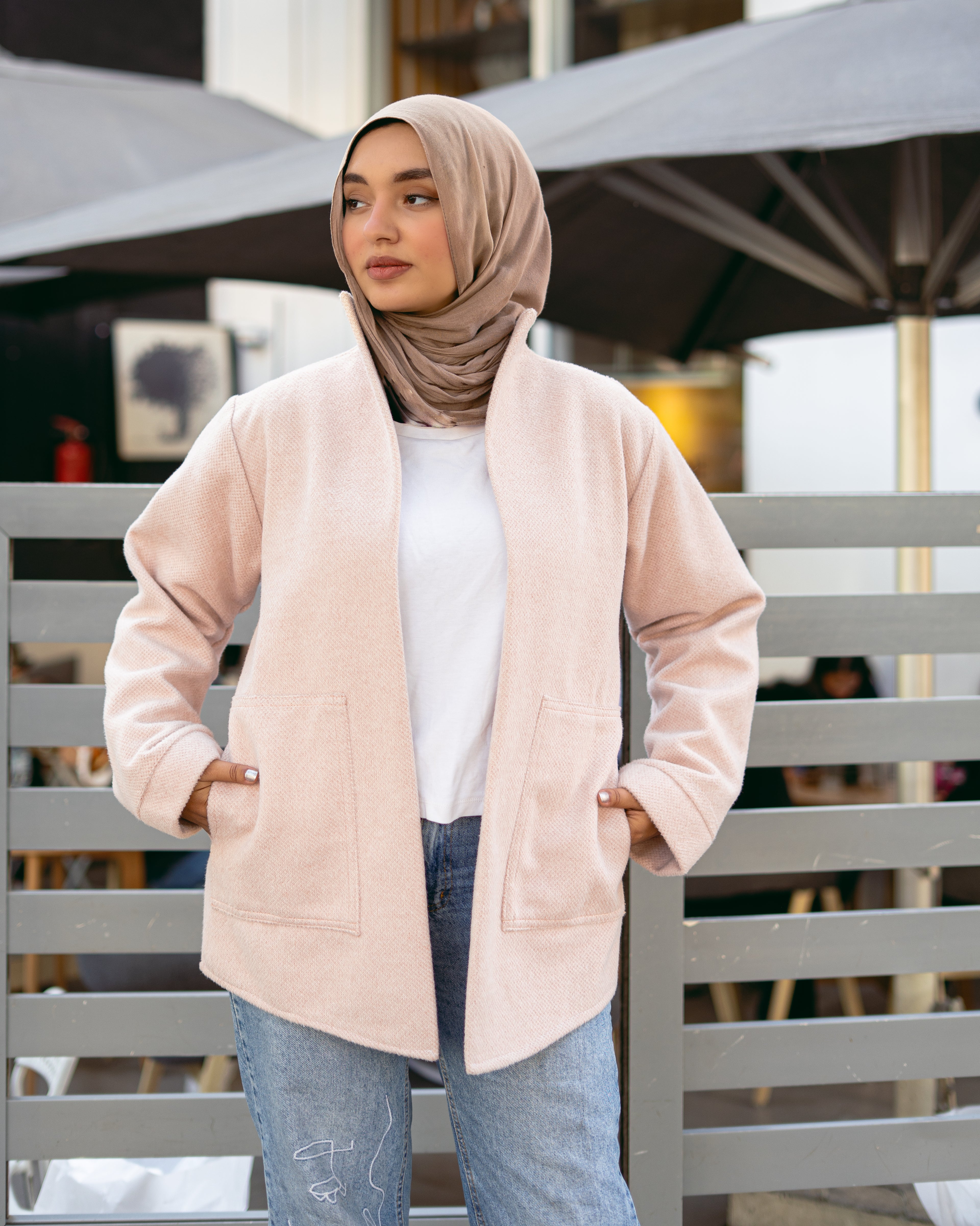 Woman wearing a beige jacket and hijab standing outdoors with blurred background