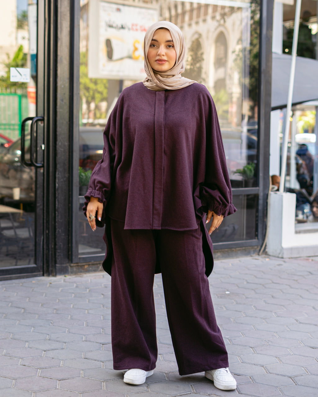 Woman wearing a purple outfit with a hijab standing on a street.