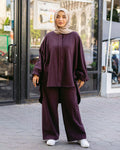 Woman wearing a purple outfit with a hijab standing on a street.